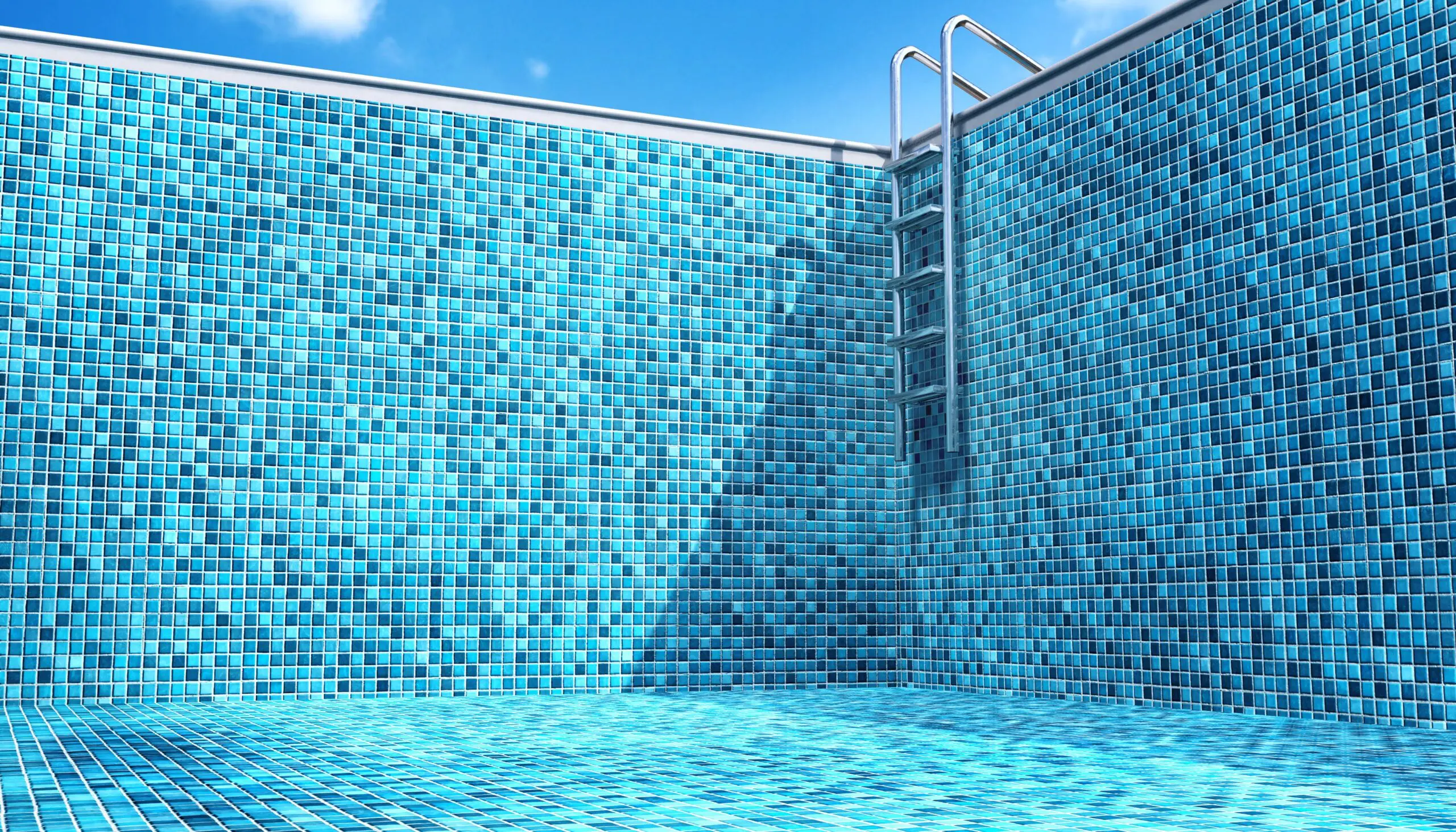 Empty swimming pool with blue mosaic tiles covering the walls and floor, metal ladder at the deep end, and a clear blue sky overhead.